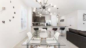 A modern kitchen with dark cabinets, a central island, and a dining area with a glass table and chairs.