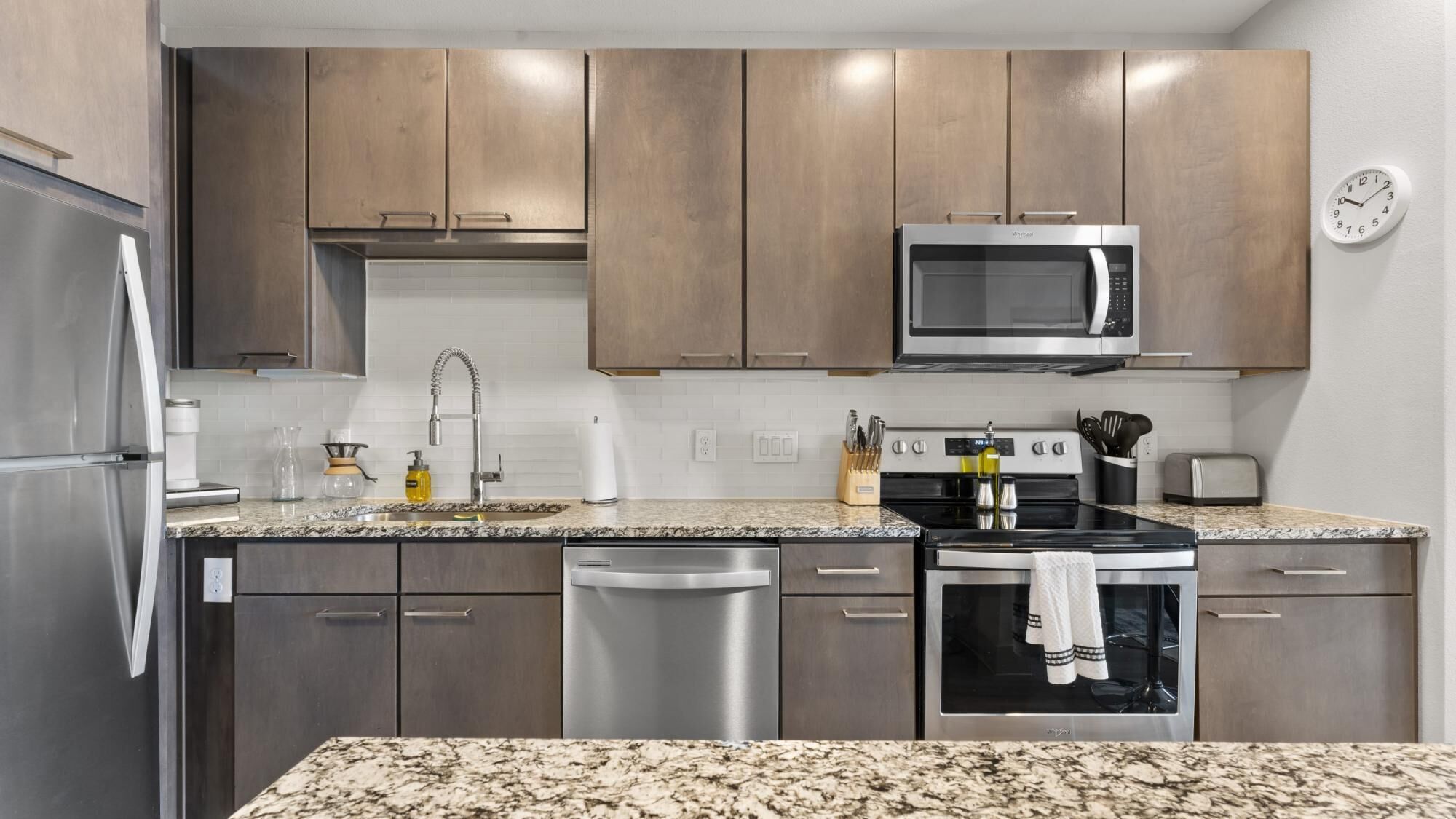 A modern kitchen with stainless steel appliances, wooden cabinets, and a granite countertop.