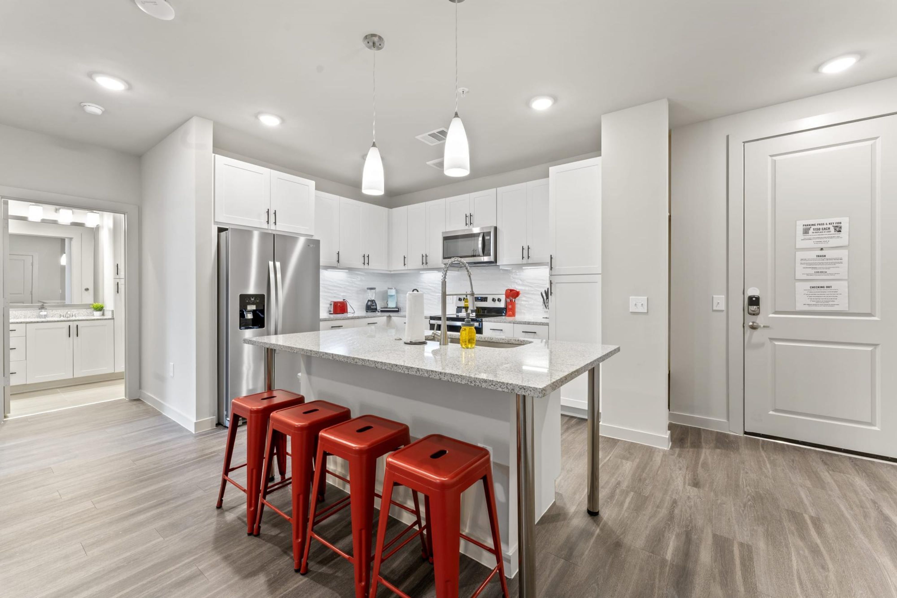 A modern kitchen with white cabinets, stainless steel appliances, and a central island with red bar stools.