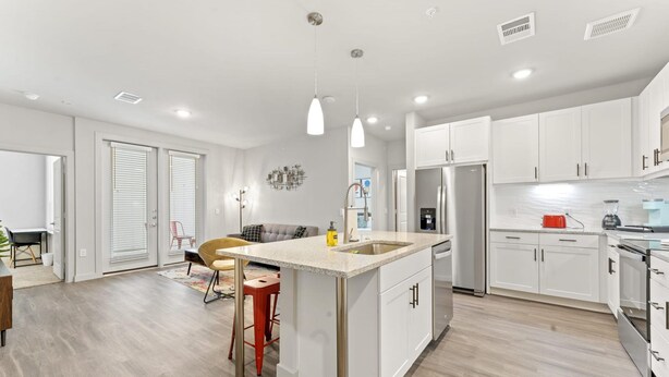 A modern kitchen with white cabinets, a central island, stainless steel appliances, and pendant lighting.