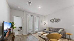 A modern living room with a flat-screen TV, a grey sofa, a yellow armchair, and a coffee table. - Prime Soco Charming 1BR King Suite w Pool Parking (Austin)