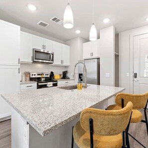 A modern kitchen with white cabinets, a granite countertop, stainless steel appliances, and two yellow chairs.