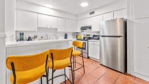 A modern kitchen with white cabinets, a stainless steel refrigerator, and two yellow bar stools. - Prime Soco Airy 1BR King Suite w Pool Parking (Austin)