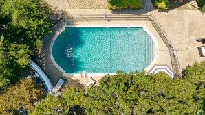An aerial view of a rectangular swimming pool with a surrounding deck, surrounded by trees and a stone wall. - Prime Soco Airy 1BR King Suite w Pool Parking (Austin)