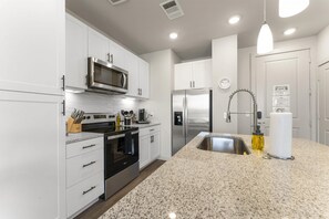 Uma cozinha moderna com armários brancos, eletrodomésticos de aço inoxidável, bancada de granito e forno embutido.