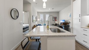 A modern kitchen with granite countertops, a stainless steel sink, and a dining area with a bar stool.