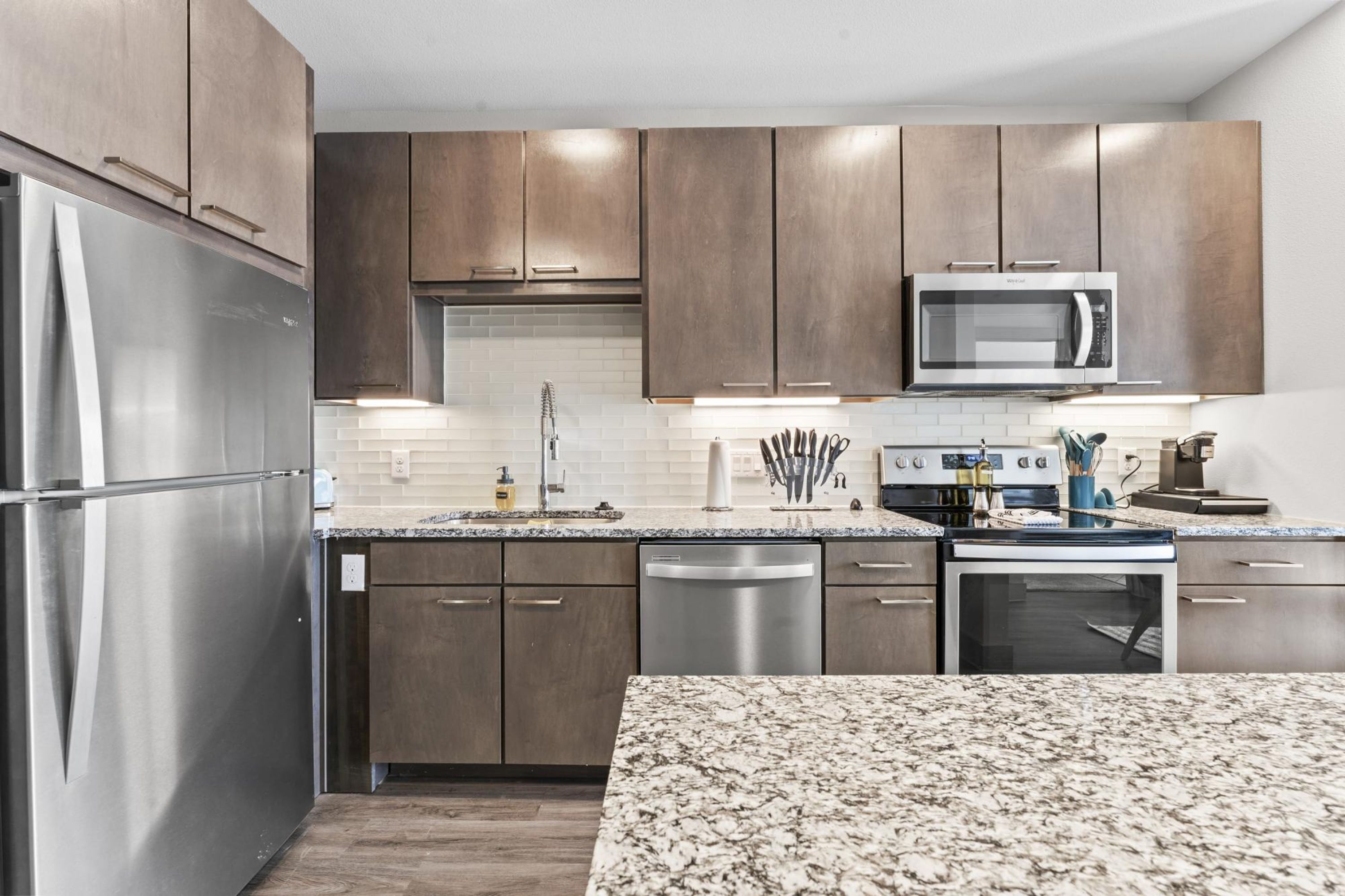 A modern kitchen with stainless steel appliances, wooden cabinets, and a granite countertop.