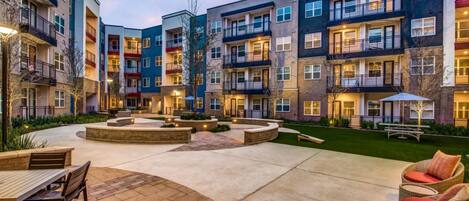 A multi-story residential building with balconies, a courtyard with seating, and a well-maintained lawn.