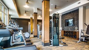 Ein Fitnessraum mit Laufbändern, Kraftgeräten und einem Fernseher an der Wand.