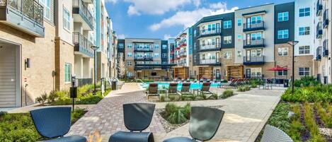 A courtyard with outdoor seating, a fire pit, and a pool area surrounded by multi-story residential buildings.