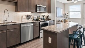 A modern kitchen with dark wood cabinets, stainless steel appliances, and a central island with bar stools. - Cozy 1BR King Suite Close to Downtown w Fast Wifi (Austin)