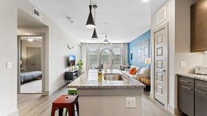 A modern kitchen with a central island, a dining area with a sofa, and a living space with a TV. - Serene 1BR King Suite Close to Downtown w Fast Wifi (Austin)