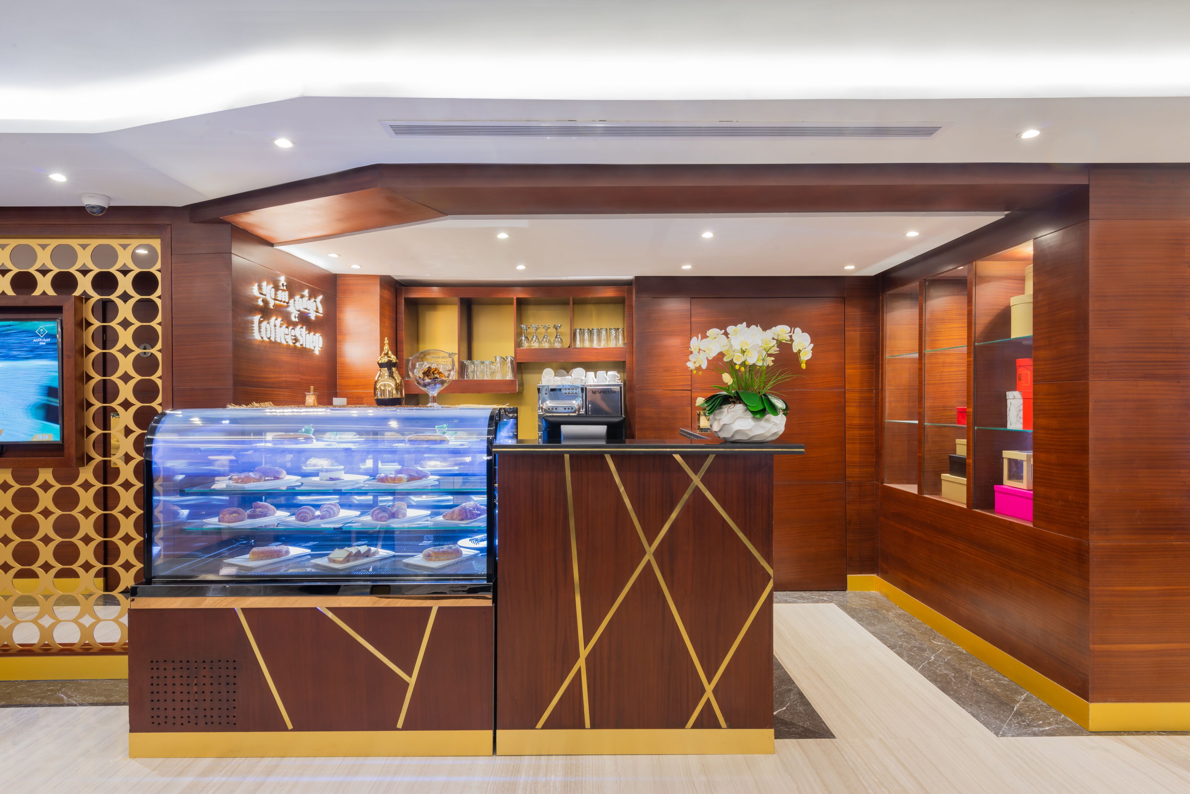 Un comptoir de boulangerie avec une vitrine remplie de pâtisseries, une machine à café et une orchidée décorative.