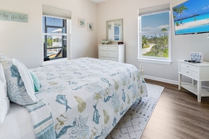 A bedroom with a bed, a dresser, a TV, and a window with a view of a beach.