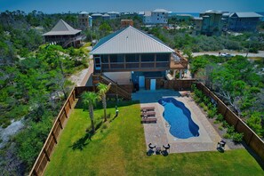 A large house with a swimming pool, surrounded by a wooden deck and a fenced yard.