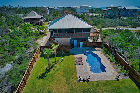 A large house with a swimming pool, surrounded by a wooden deck and a fenced yard.