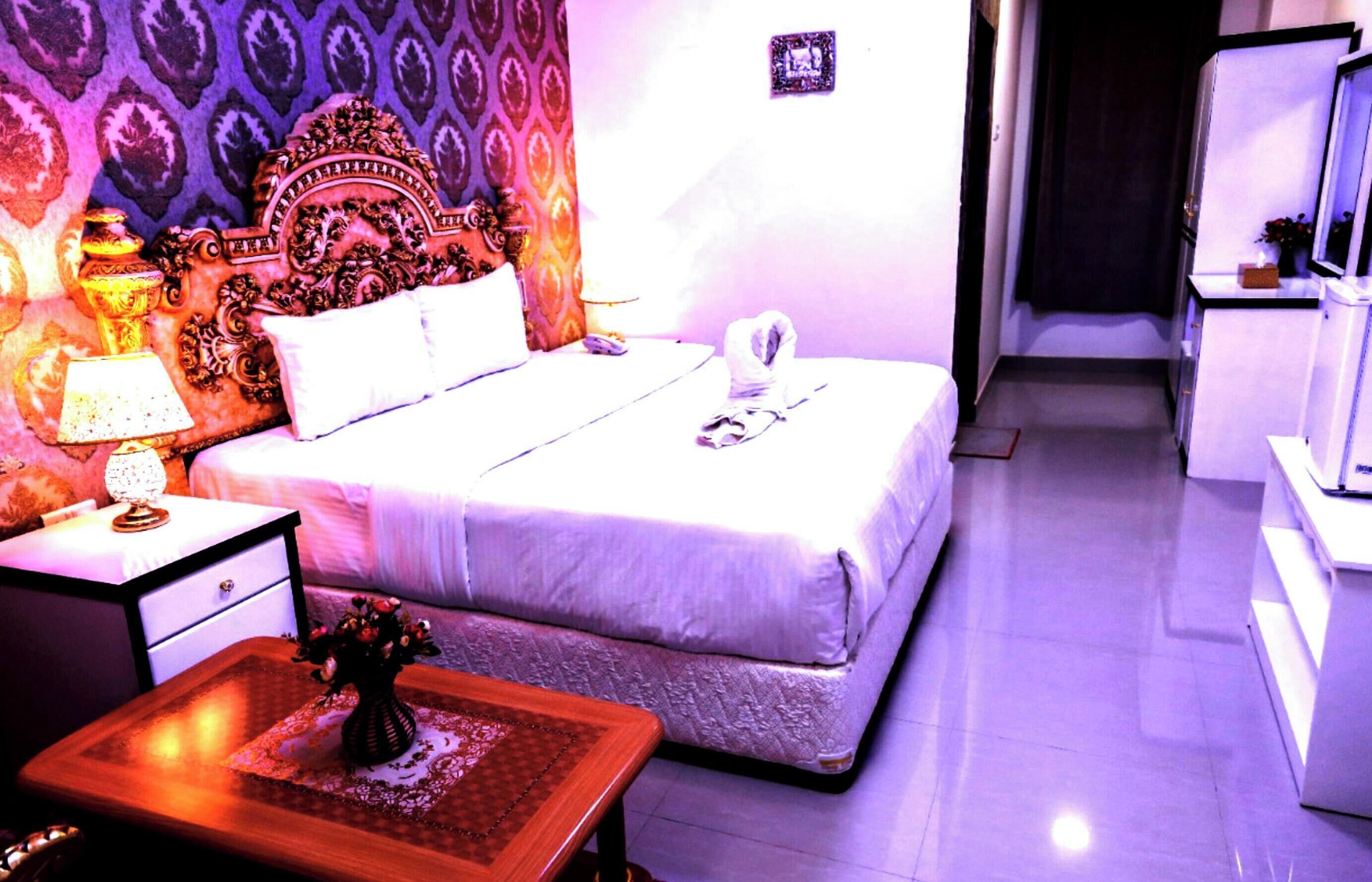 A hotel room with a bed, bedside table, lamp, and a small table with a vase.