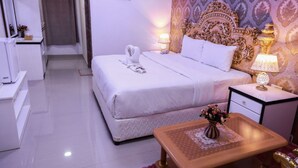 A hotel room with a neatly made bed, a bedside table with a lamp, a small table with a vase of flowers, and a decorative headboard.