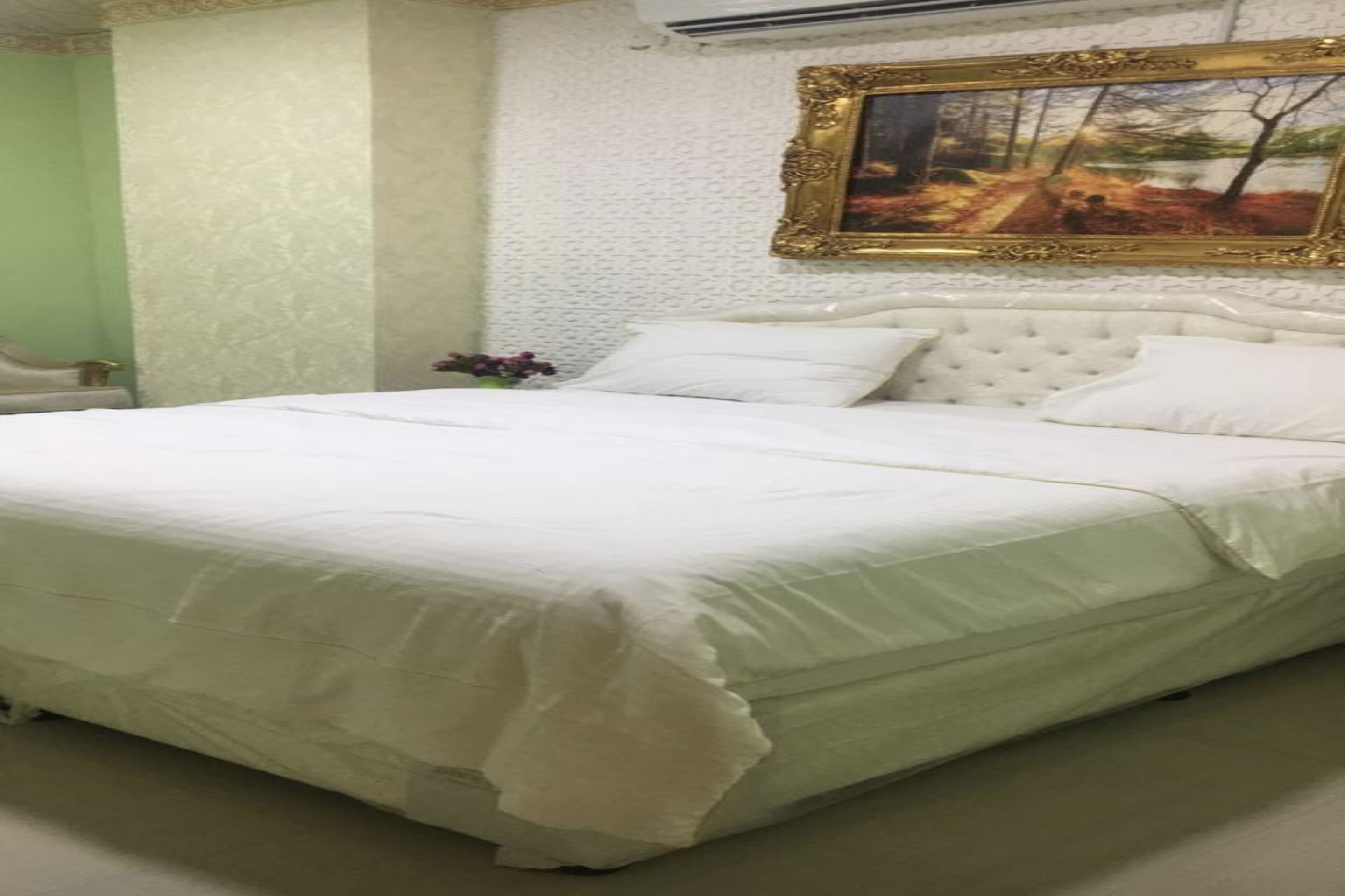 A neatly made bed with a white bedspread and pillows, a tufted headboard, and a framed painting on the wall.