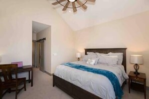 A bedroom with a bed, bedside tables, a desk, and a ceiling fan.