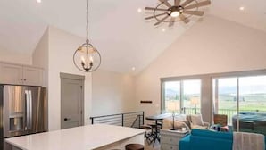 A modern kitchen with a central island, bar stools, and a ceiling fan. - New Cool 4BR Mountain Home: Views, Games, Hot Tub (Granby)