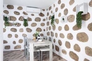 Zona pranzo con parete decorata con motivo in pietra, condizionatore d'aria bianco e tavolo con sedie.
