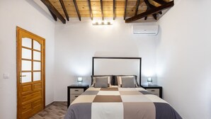 Ein Schlafzimmer mit kariertem Bettüberwurf, Holztür und Decke mit sichtbaren Balken.