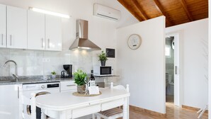 A modern kitchen with white cabinetry, a stainless steel range hood, a microwave, and a dining table with chairs. - Casa Maria with Roque Nublo view (Tejeda)