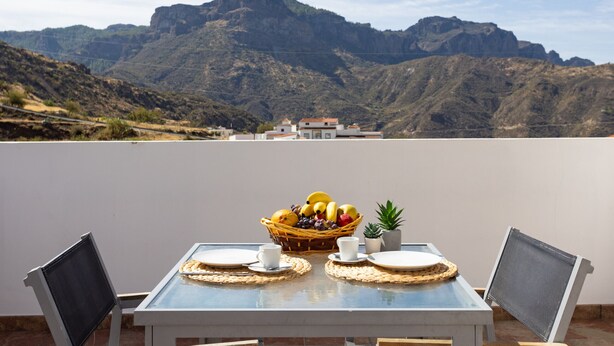 A table with a fruit basket, two cups, and a small plant on a terrace with a mountain view. - Casa Maria with Roque Nublo view (Tejeda)