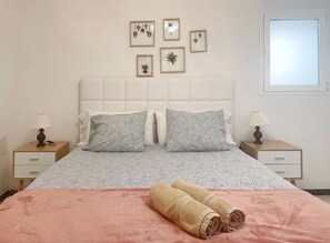 Un letto rifatto con cura, lenzuola a fantasia, due comodini con lampade e stampe botaniche incorniciate alle pareti.