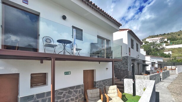 A modern building with a balcony, outdoor seating, and a stone wall. - Casa Maruca with Roque Nublo view (Tejeda)