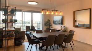 Ett modernt matområde med ett stort bord och stolar, en hängande lampa och utsikt genom stora fönster.
