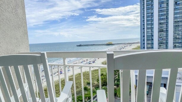 Ein Balkon mit weißen Stühlen mit Blick auf einen Strand und einen Steg.