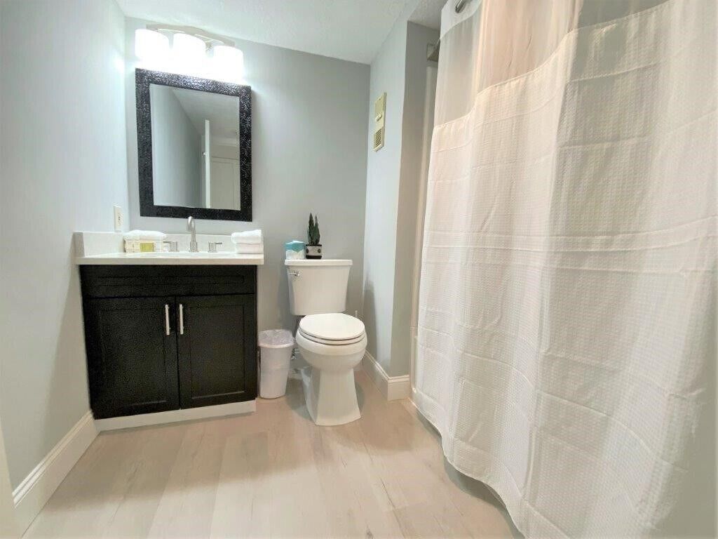 A bathroom with a white toilet, black cabinets, a mirror, and a shower curtain.