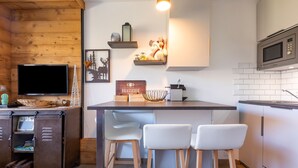 A modern kitchen with wooden cabinets, a microwave, and a bar area with stools. - Résidence Le Necou - Les Ménuires (Les Belleville)