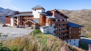 A multi-story hotel with a stone facade, wooden balconies, and a parking area. - Résidence Le Necou - Les Ménuires (Les Belleville)