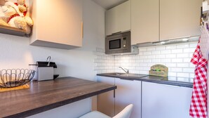 A kitchen with white cabinets, a microwave, a sink, and a wooden shelf with a teddy bear. - Résidence Le Necou - Les Ménuires (Les Belleville)