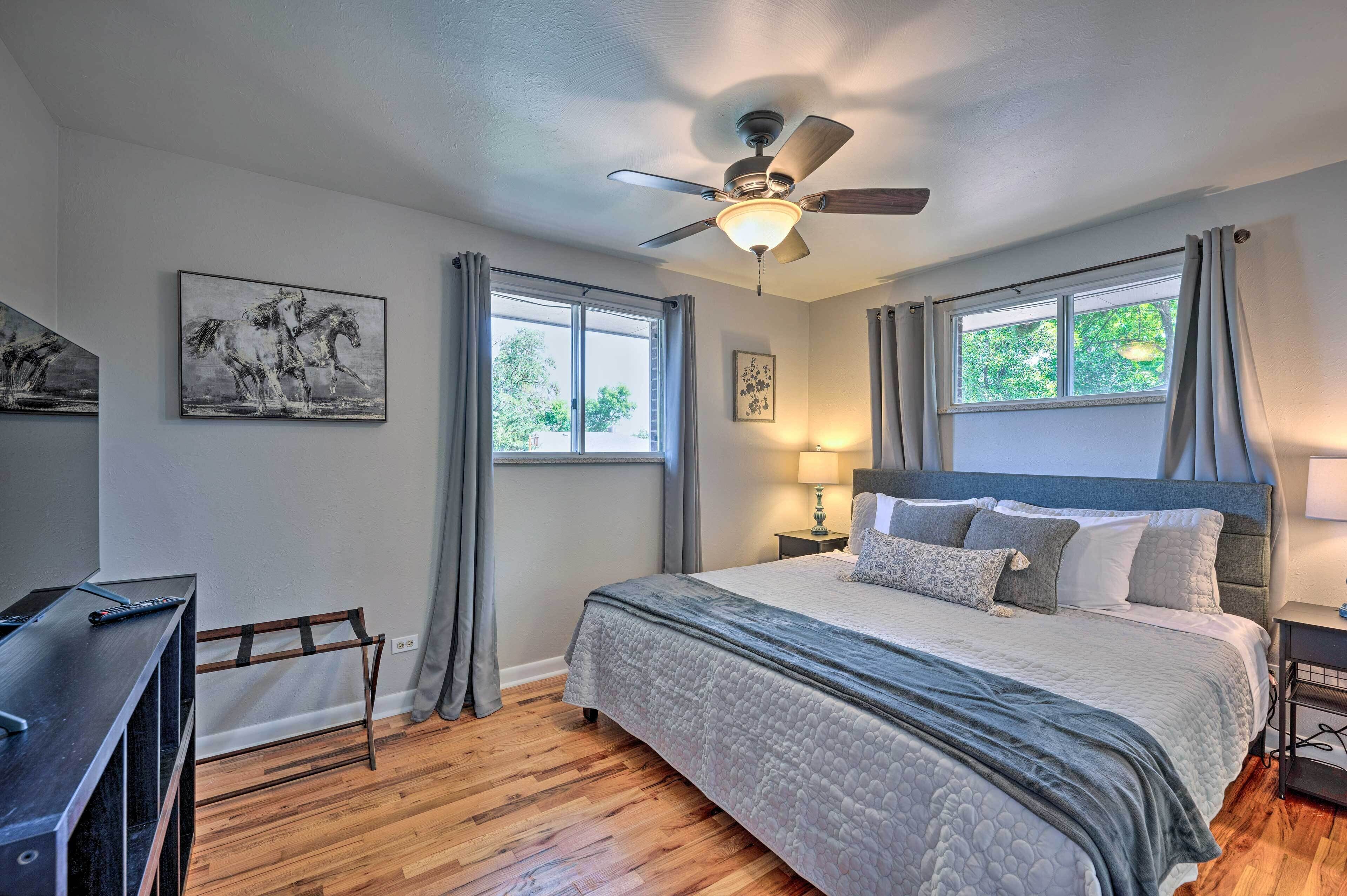A bedroom with a bed, a desk, a ceiling fan, and two windows.