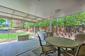Eine Terrasse im Freien mit rundem Tisch und Stühlen, einem Grill und Blick auf einen Garten durch einen überdachten Bereich.