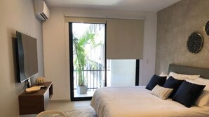 Une chambre moderne avec un lit, une télévision, une petite table avec un vase et un balcon offrant une vue sur les palmiers.