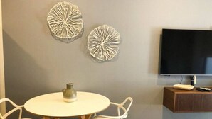 Un salon moderne avec une table ronde, deux chaises blanches, un petit vase et un téléviseur à écran plat fixé au mur.