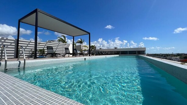 Une piscine à l’eau d’un bleu cristallin, un espace détente abrité avec des chaises longues, et une vue sur le paysage environnant.