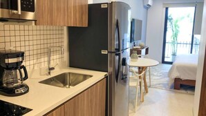 Une cuisine moderne équipée d’un four à micro-ondes encastré, d’un réfrigérateur en acier inoxydable et d’une machine à café. Un petit coin repas avec une table et des chaises est également disponible.