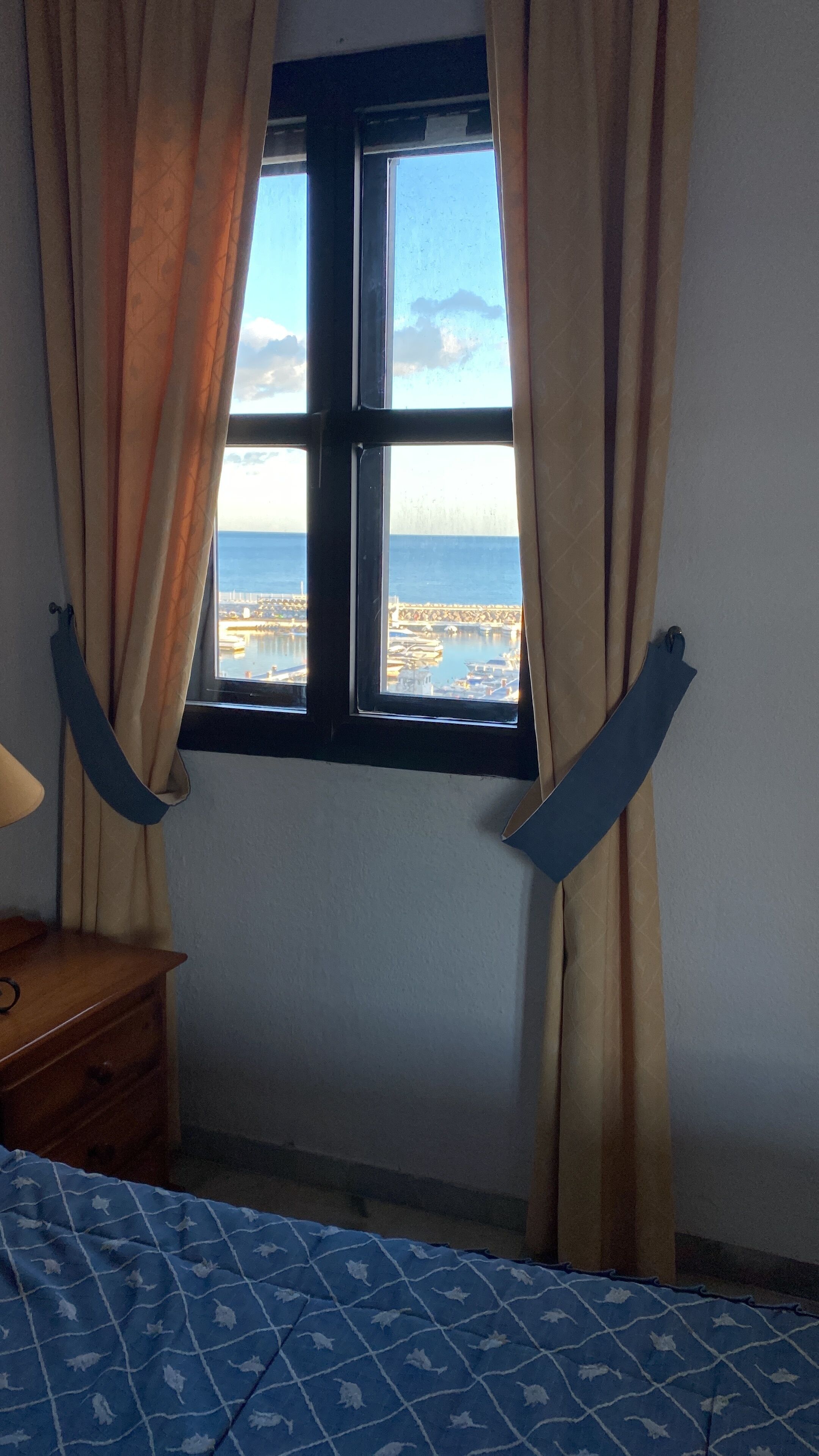Ein Zimmer mit einem Bett, einem Nachttisch aus Holz und einem Fenster mit Vorhängen.