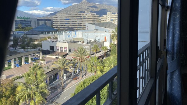 Une vue d’une ville avec ses bâtiments, ses palmiers et une montagne en arrière-plan.