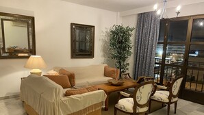 Un salon comprenant un canapé, des fauteuils, une table basse, une lampe, une plante et une grande fenêtre avec des rideaux.