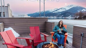 A wooden deck with red chairs, a fire pit, and a view of snow-capped mountains.