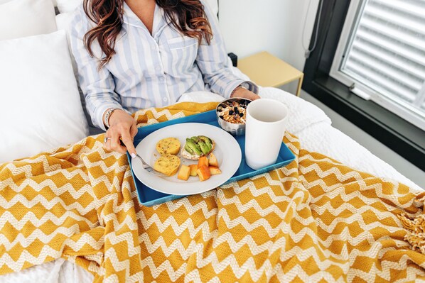 A person in bed with a tray containing food and a mug, covered with a chevron-patterned blanket.