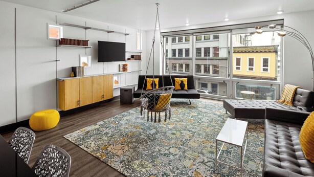 A modern living room with a sofa, a coffee table, and a hanging chair. There is a TV mounted on the wall and a window with a view of buildings.