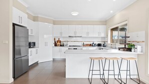 A modern kitchen with white cabinetry, a stainless steel refrigerator, a central island with bar stools, and a window with a view.